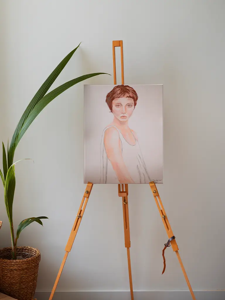 Retrato artístico de una mujer de cabello corto y expresión seria, en tonos suaves sobre un fondo neutro, colocado en un caballete de madera.