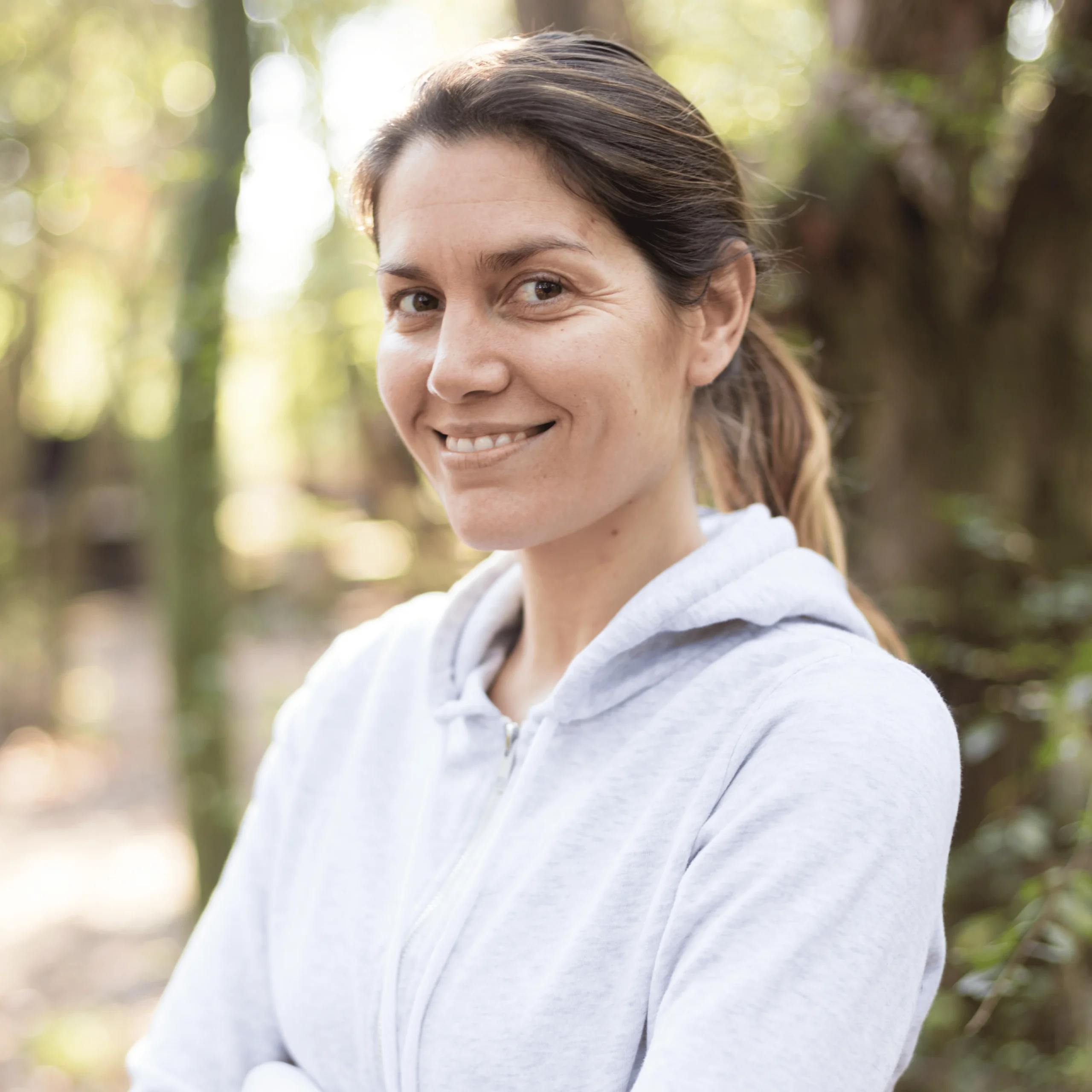 Mujer con sudadera gris sonriendo en un entorno boscoso.